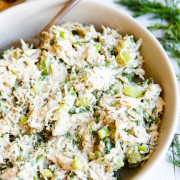 a white bowl filled with dill pickle chicken salad next to a plate of whole grain crackers