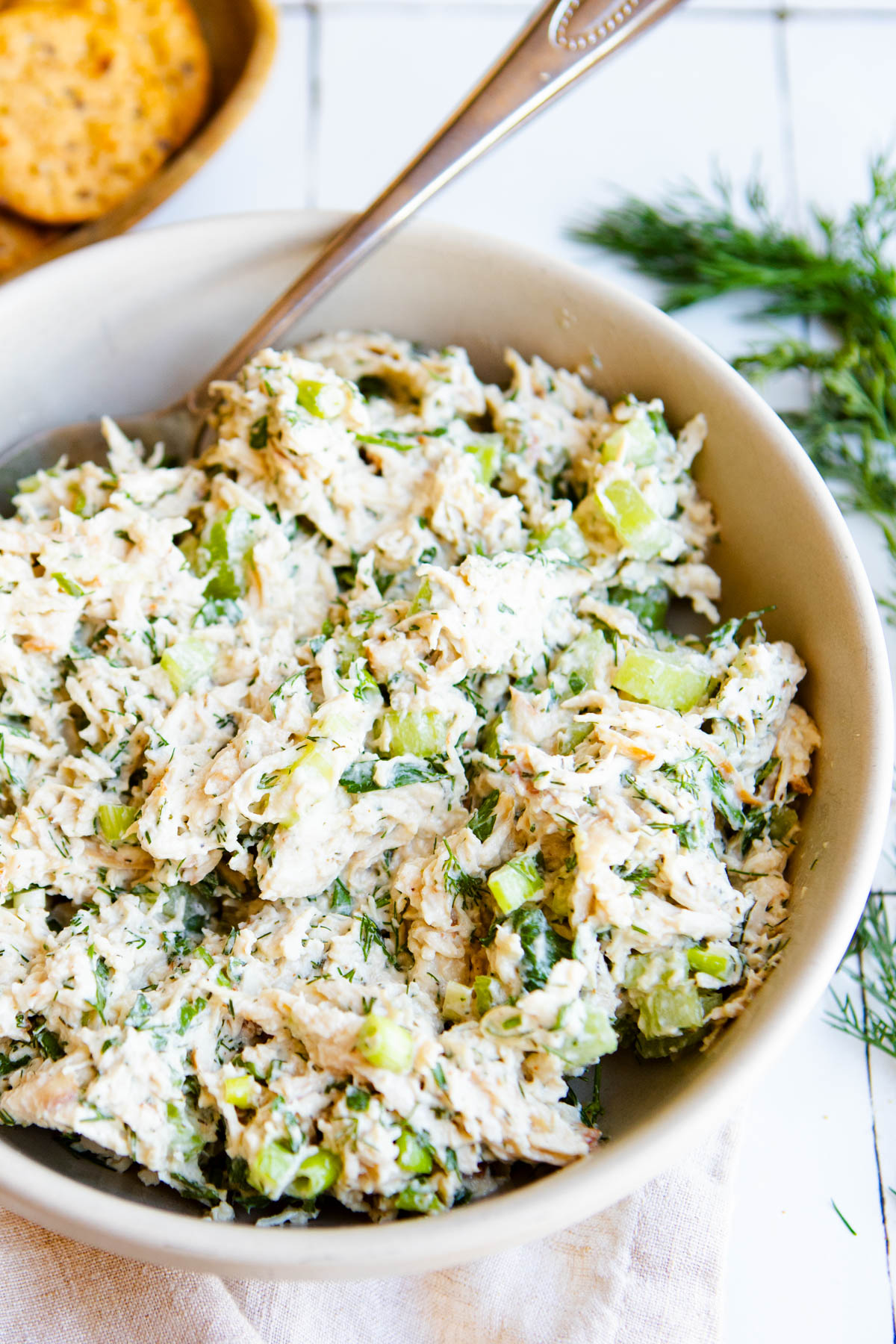 a white bowl filled with dill pickle chicken salad next to a plate of whole grain crackers 