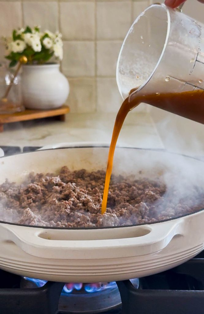sauce being added to ground beef in a skillet