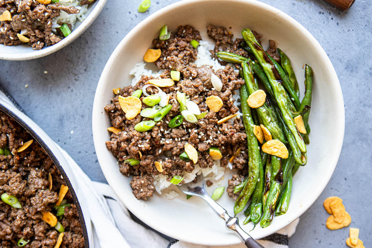 a white ceramic bowl filled with white rice and ground beef and a side of blistered green beans
