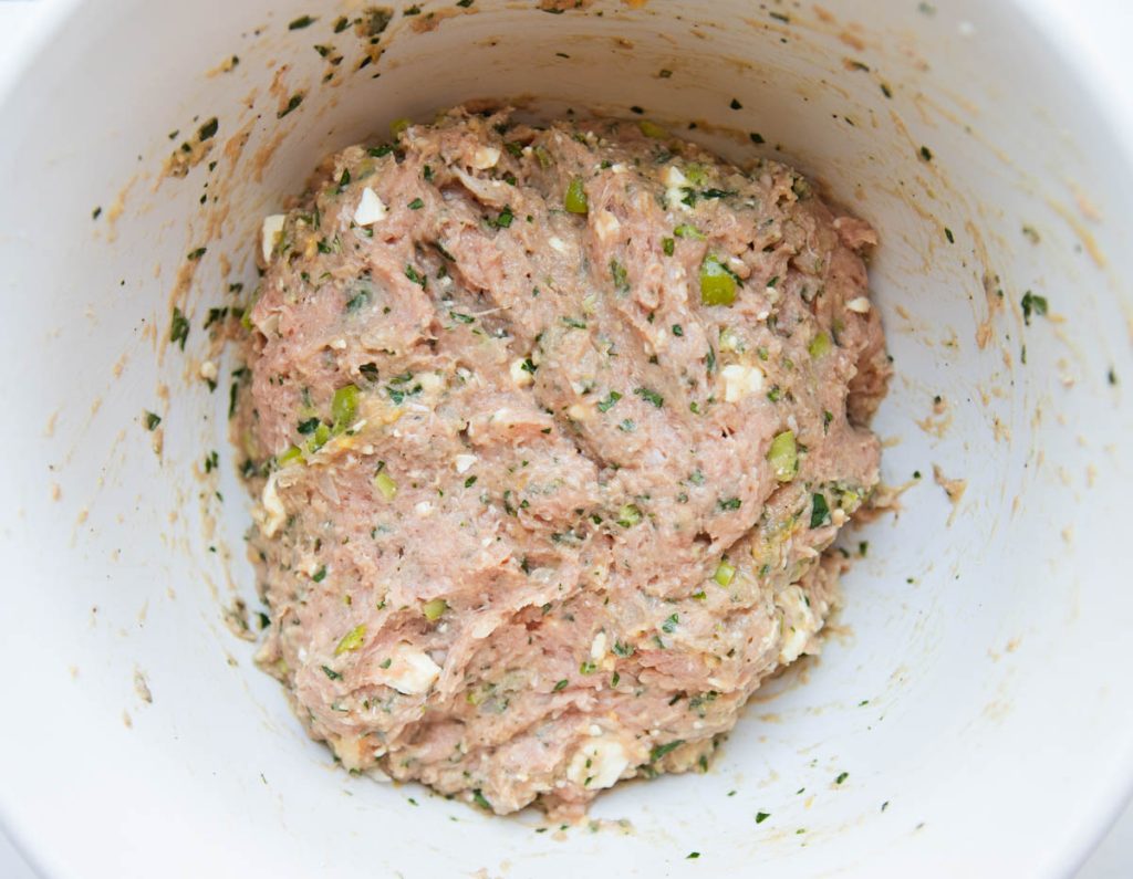 mixed ground turkey burgers with herbs and feta cheese in a white ceramic mixing bowl