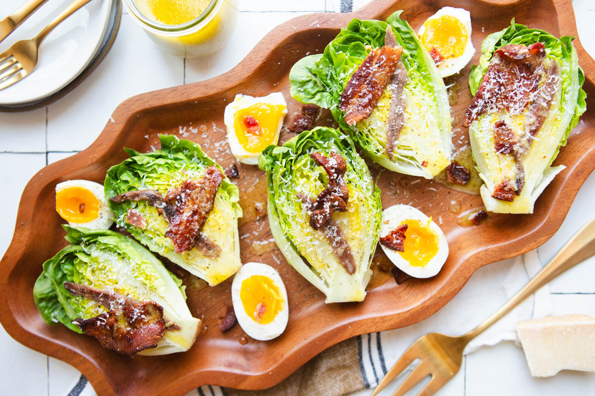 little gem salad halves served on a platter with soft-boiled eggs, bacon and anchovies