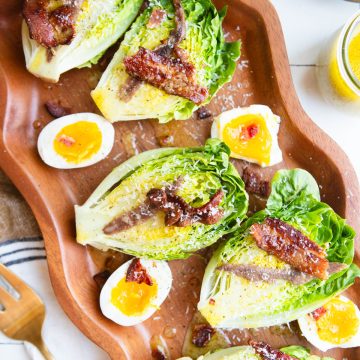 bistro salad made with little gem lettuce on a wood platter and topped with bacon and parmesan cheese