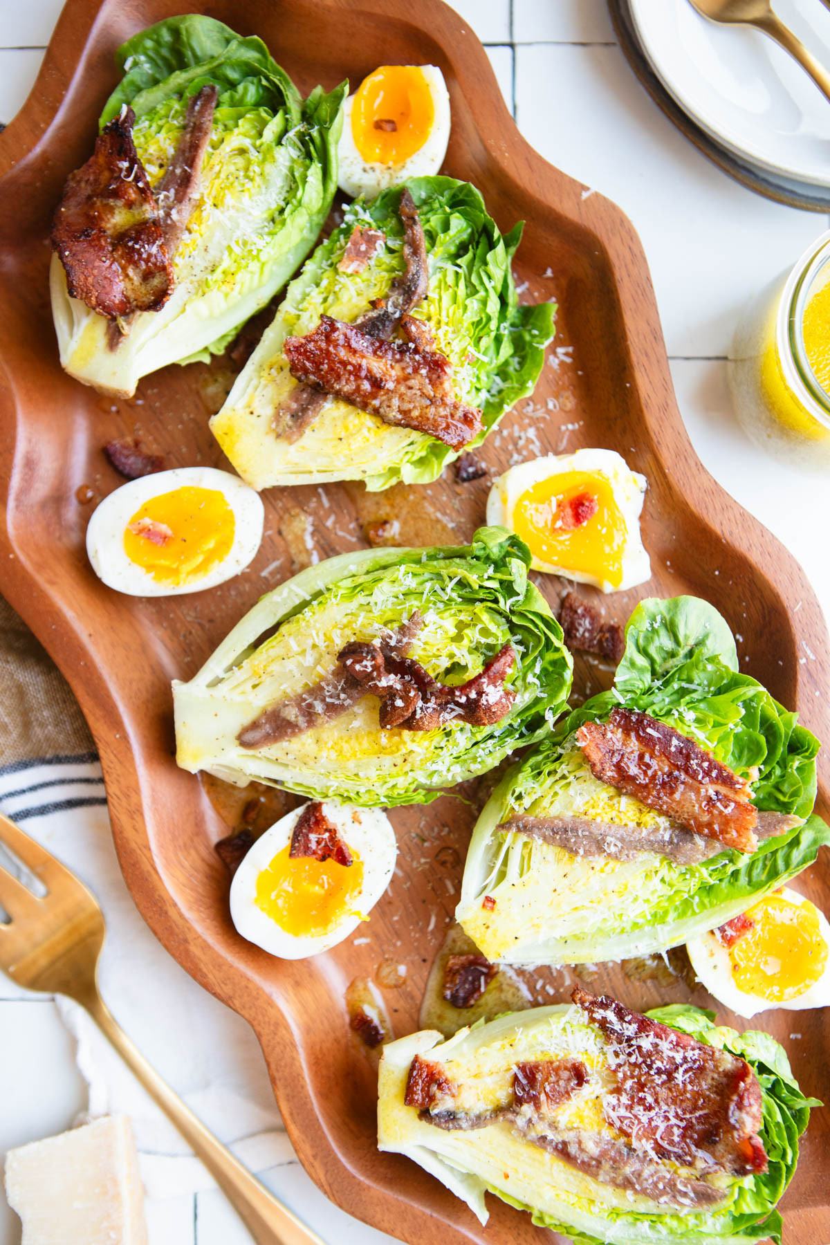 bistro salad made with little gem lettuce on a wood platter and topped with bacon and parmesan cheese