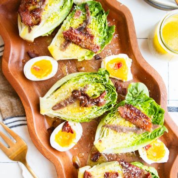 a wood platter filled with little gem lettuce halves and topped with bacon and lemon vinaigrette