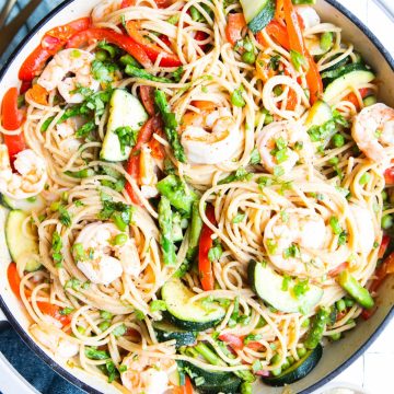 pasta primavera with veggies and shrimp in a white pan and garnished with basil
