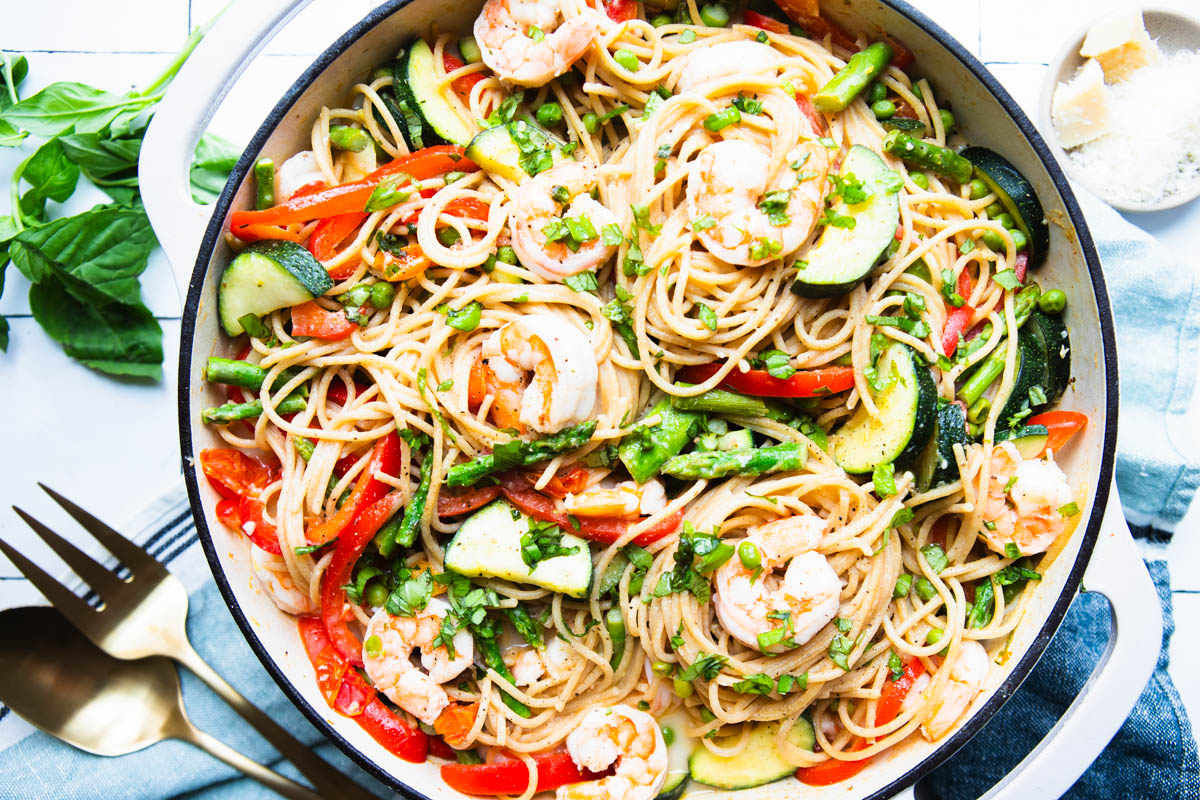pasta primavera with shrimp in a large skillet and garnished with parmesan cheese and basil
