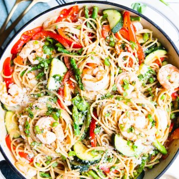 shrimp pasta primavera in a white enameled cast iron skillet garnished with parmesan cheese and basil
