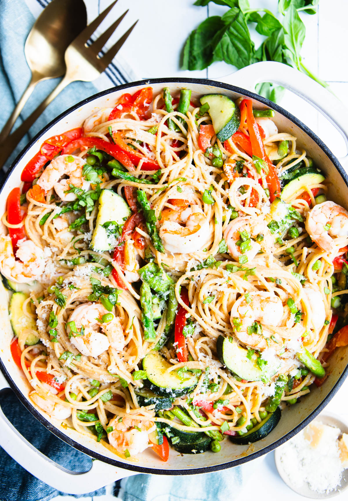 shrimp pasta primavera in a white enameled cast iron skillet garnished with parmesan cheese and basil