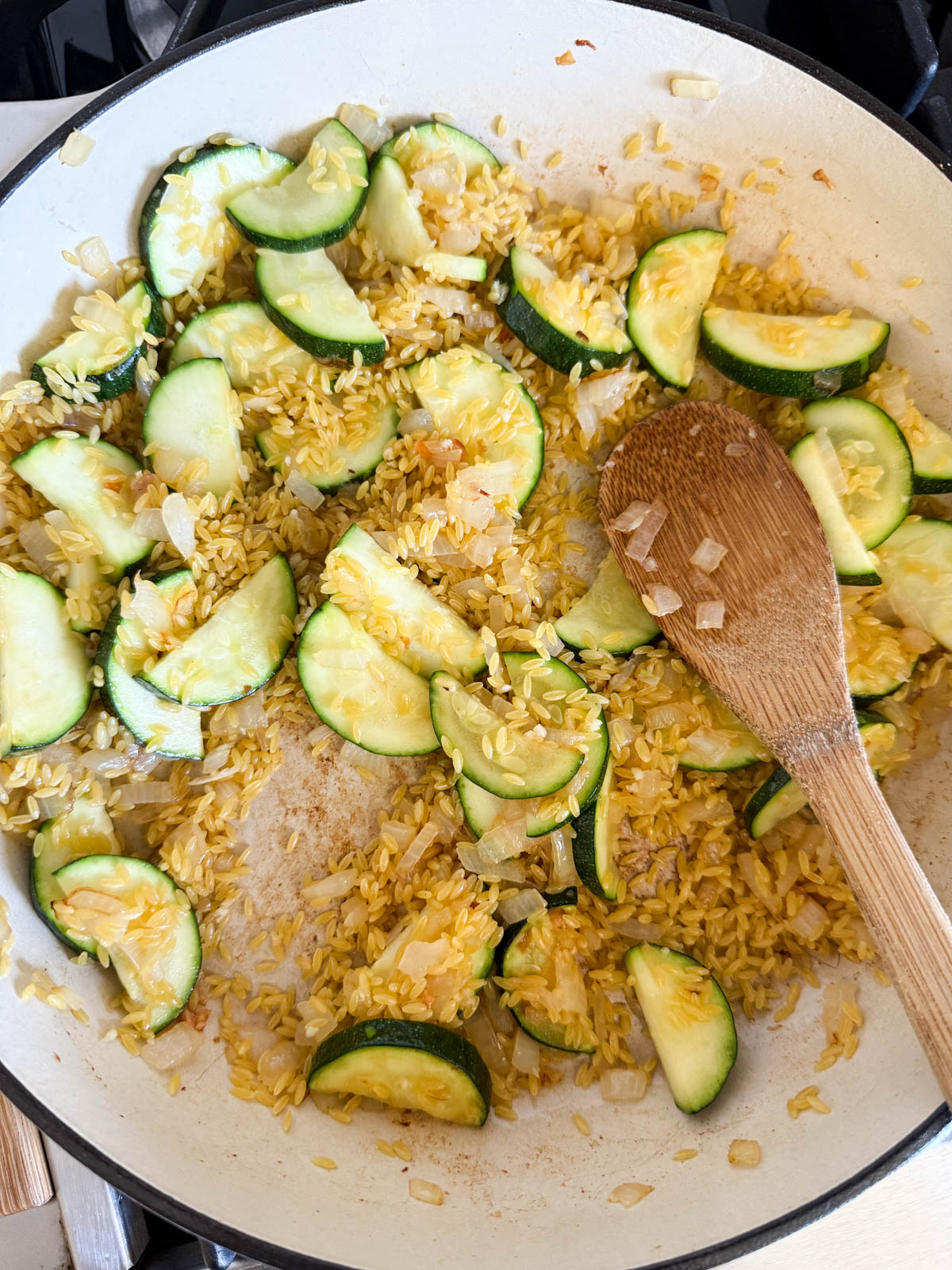 orzo added to a pan of onions and zucchini