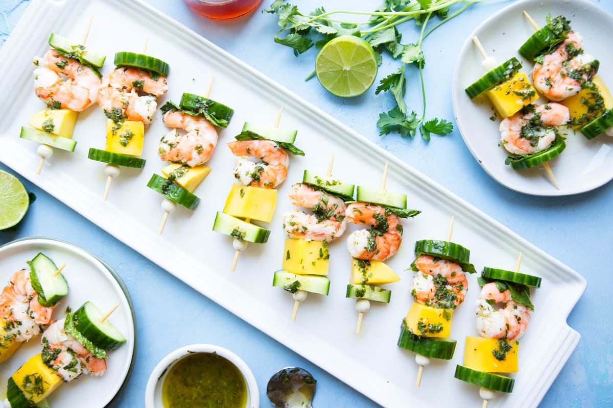 white ceramic tray filled with mini shrimp and mango skewers drizzled with cilantro lime sauce