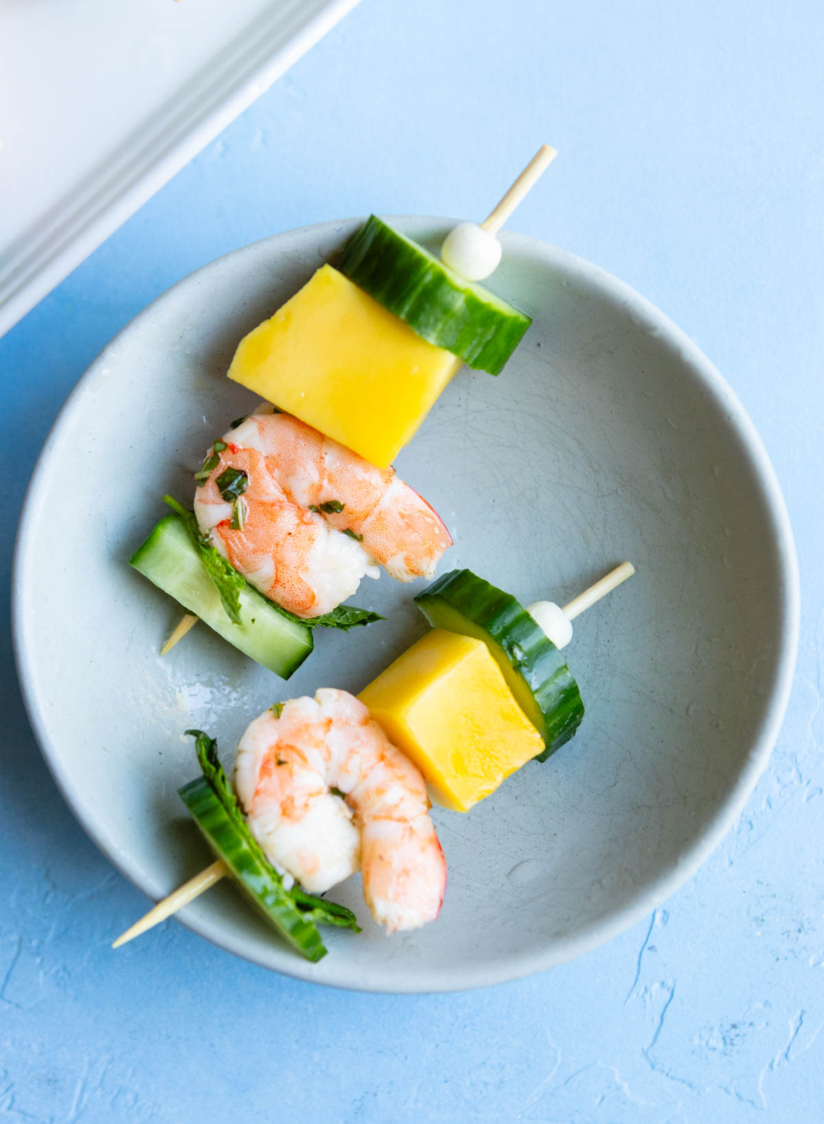 shrimp and mango and cucumber on a mini skewer setting on a small white plate
