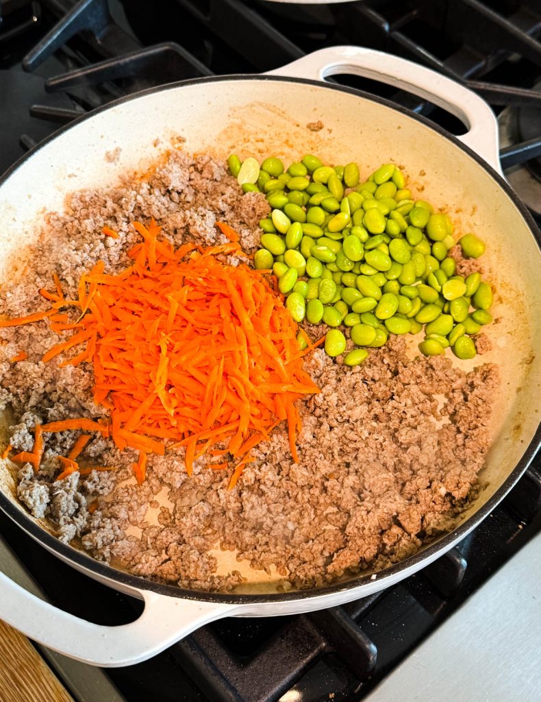 shredded carrots and edamame added to a pan of cooked ground turkey