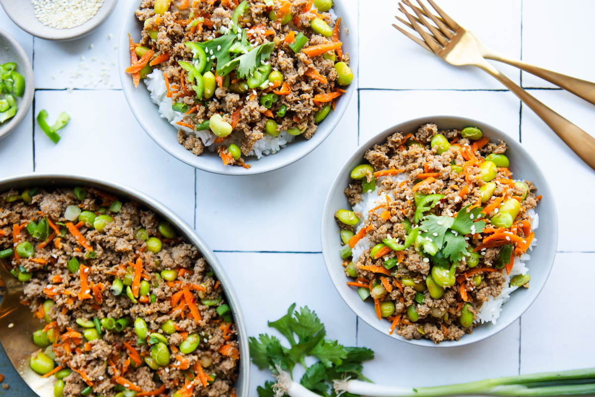 2 rice bowls topped with ground turkey and veggies and a large serving bowl with ground turkey set next to them