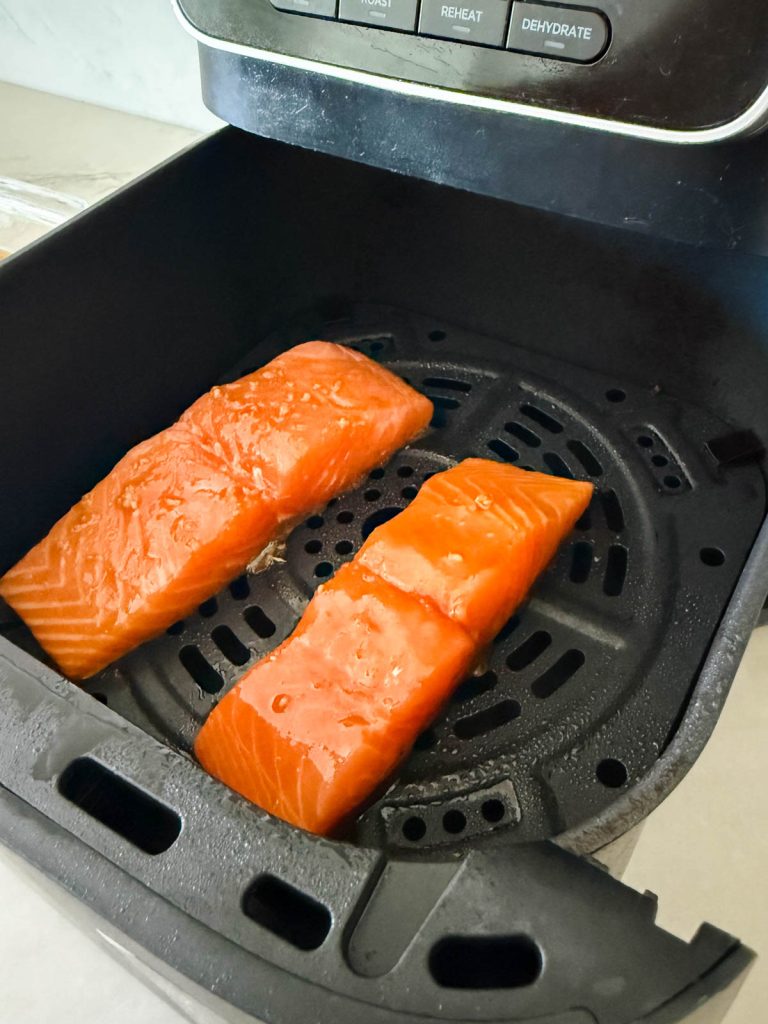 2 miso glazed salmon filets placed in an air fryer basket.