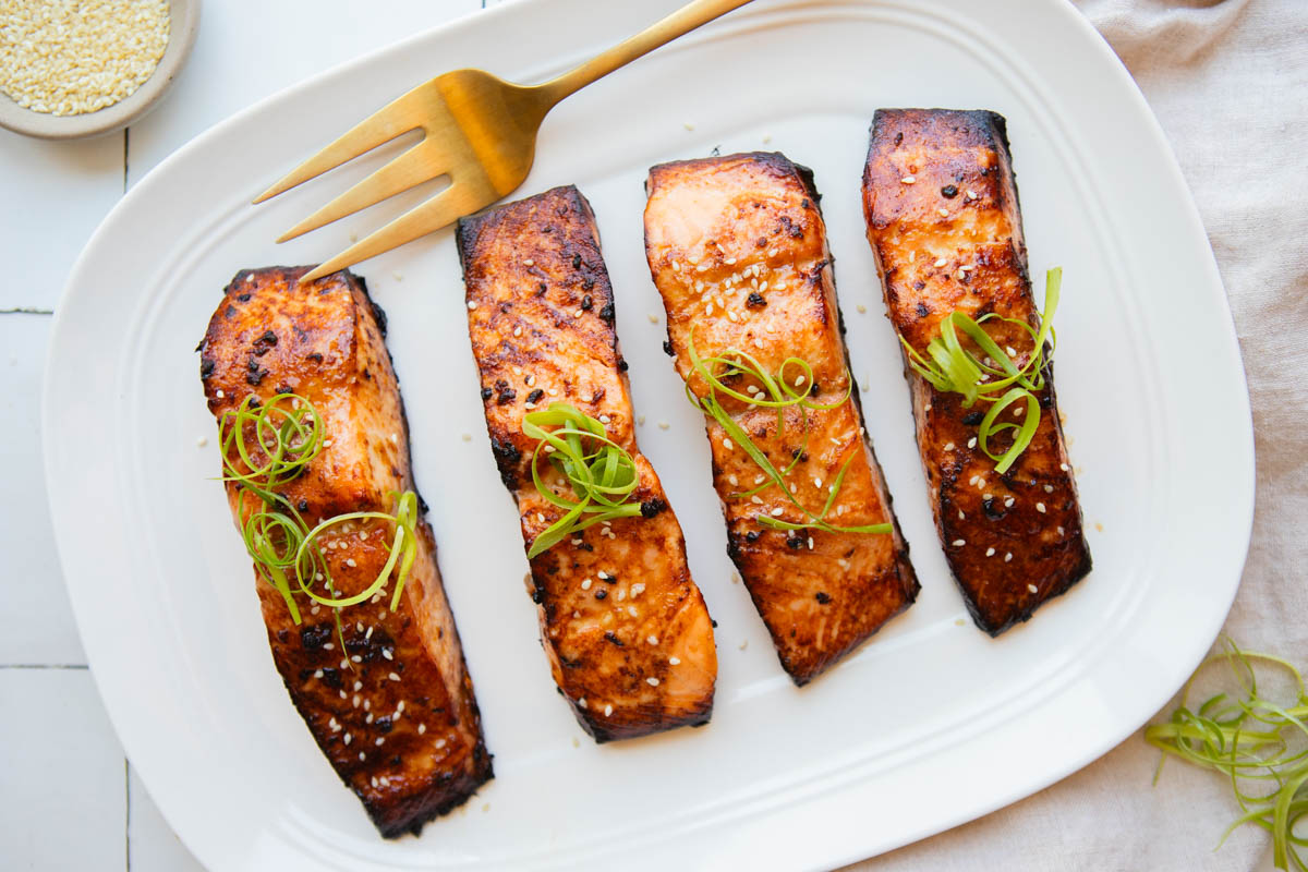 miso glazed salmon filets sprinkled with sesame seeds and a green onion garnish on a white serving platter
