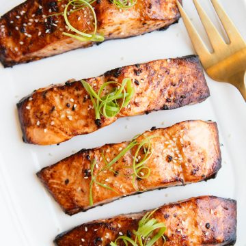 4 salmon filets cooked and served on a platter, garnished with green onion curls