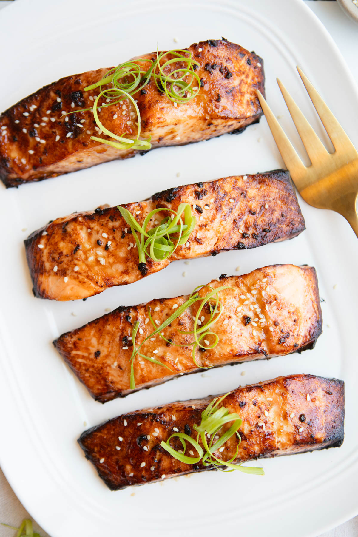 4 salmon filets cooked and served on a platter, garnished with green onion curls
