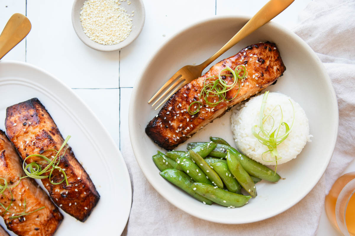 a platter and bowl filled with salmon filets cooked in the air fryer with a miso honey glaze, next to a bowl of rice and sugar snap peas