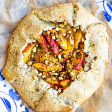 a rustic peach galette with herbs and pistachios is served on a parchment lined blue and white French platter