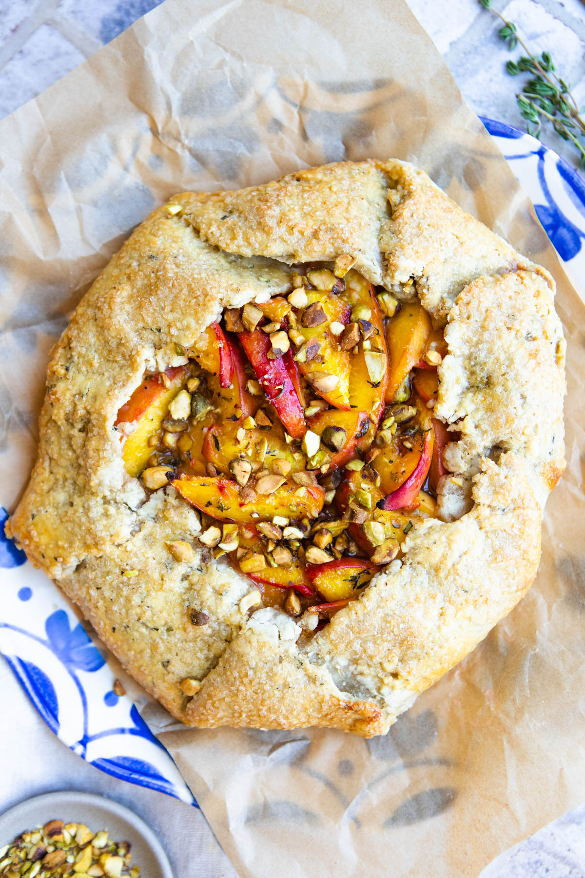 a rustic peach galette with herbs and pistachios is served on a parchment lined blue and white French platter