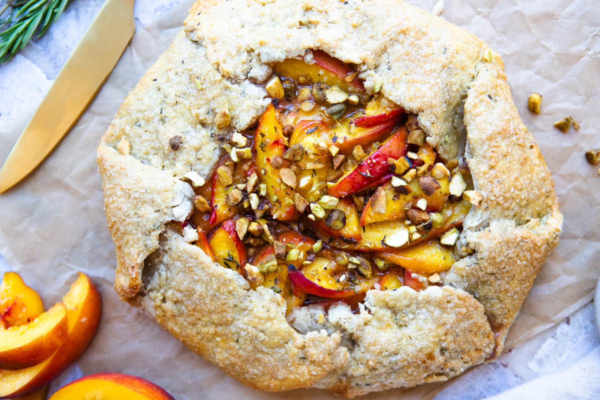 French peach galette with an olive oil crust baked on a parchment paper with crushed pistachios on top