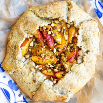 rustic peach galette with an olive oil crust and chopped pistachios on a blue and white floral serving plate