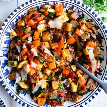 blue and white ceramic bowl filled with easy ratatouille and garnished with parsley and shaved parmesan cheese