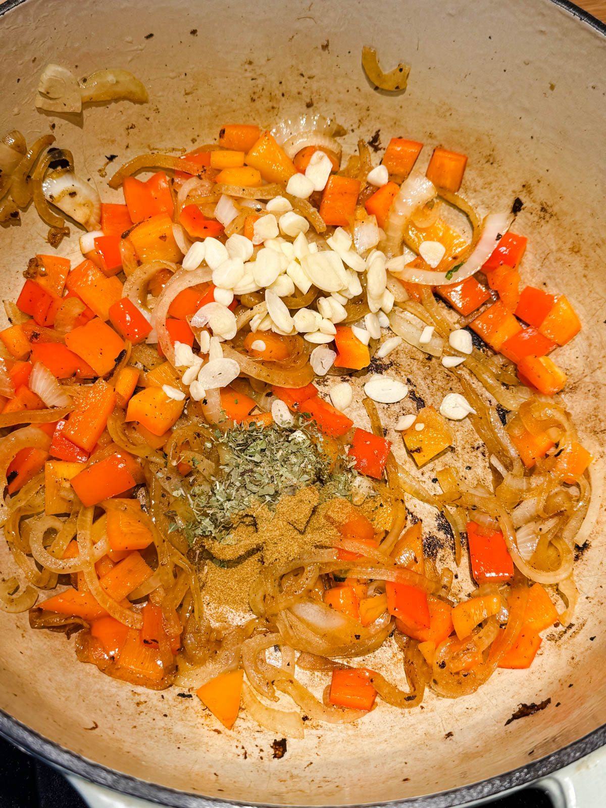 garlic and dried herbs and seasonings added to a large Dutch oven filled with cooked peppers and onions
