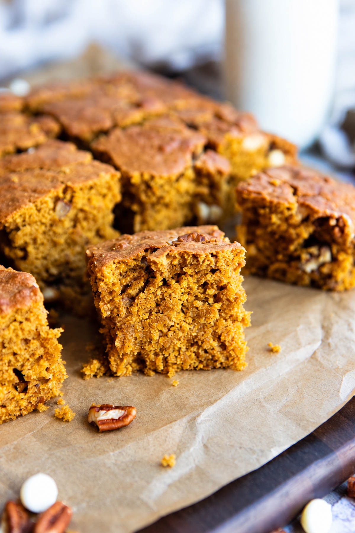 moist pumpkin bars with white chocolate chips and pecans on a parchment lined wood board